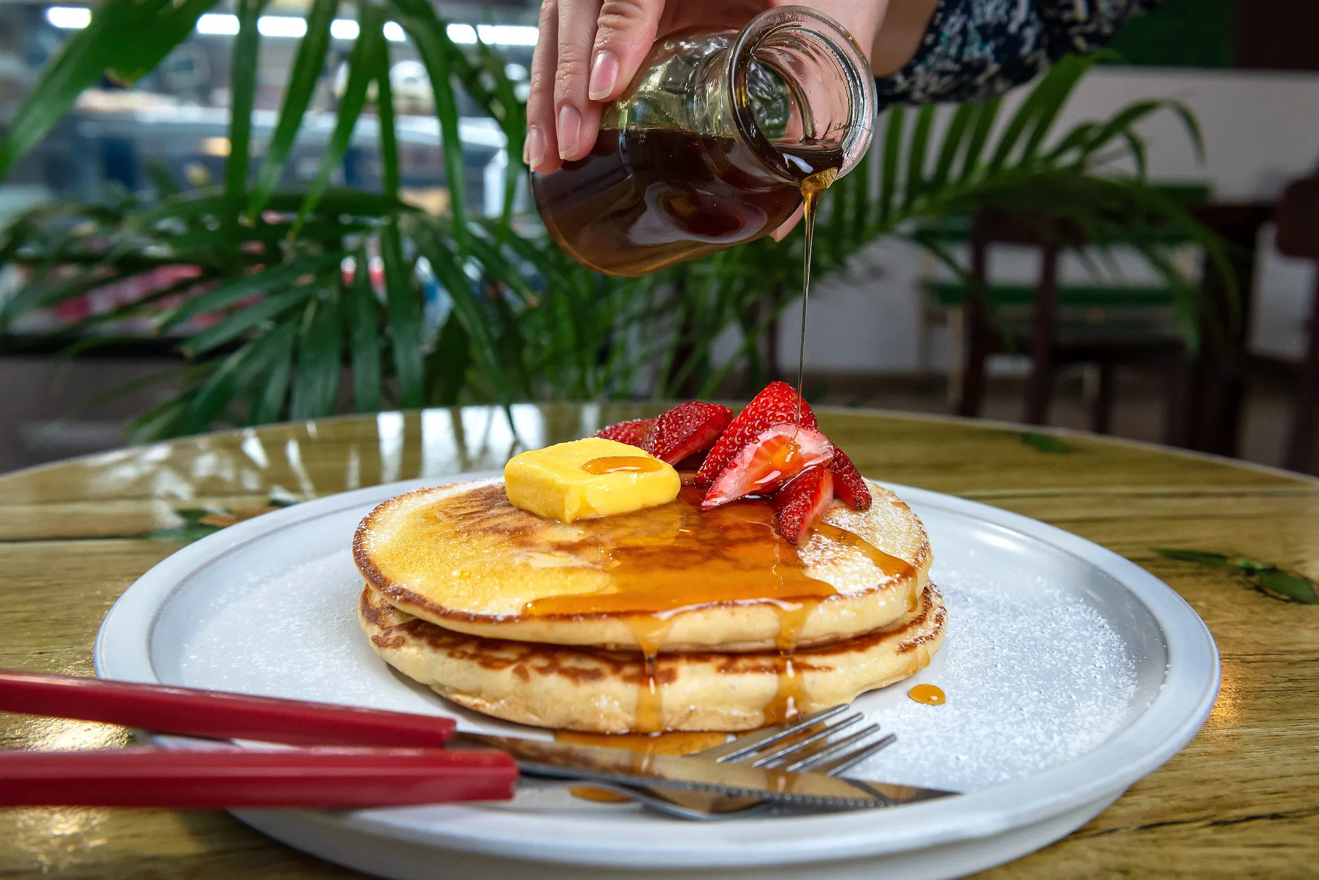 Pancakes con fresas y mantequilla mientras les sirven miel